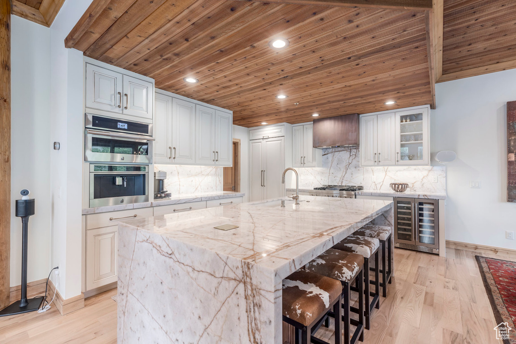Kitchen with wine cooler, a sink, wooden ceiling, light wood-style floors, and baseboards