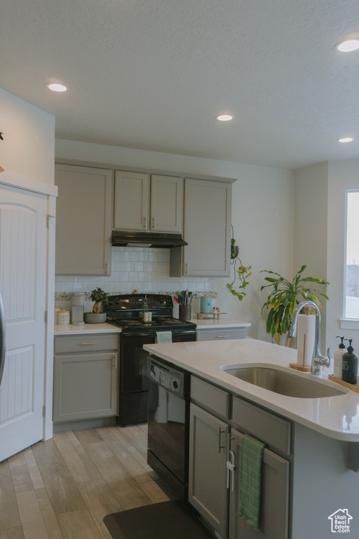 Kitchen with a sink, gray cabinetry, under cabinet range hood, black appliances, and light countertops