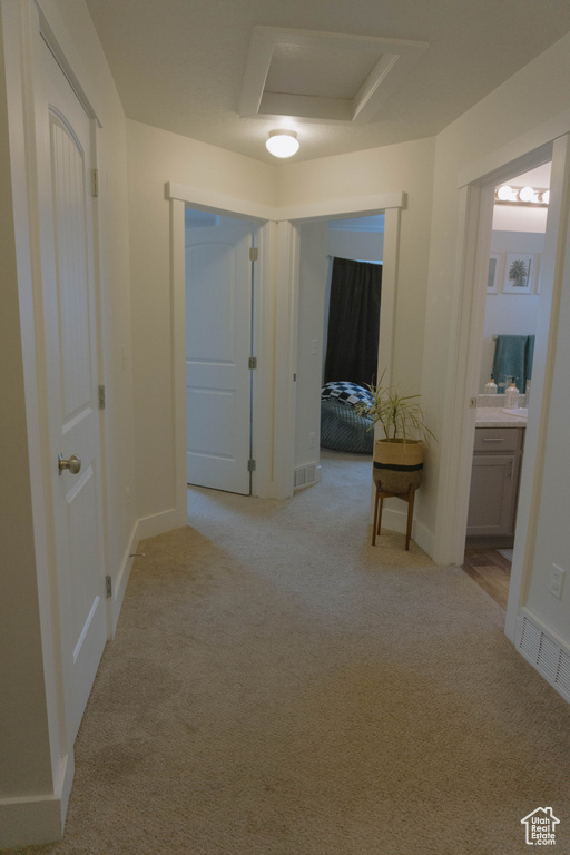 Hallway featuring attic access, light carpet, and baseboards