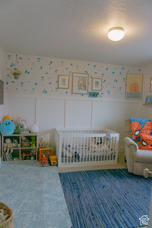 Bedroom with wallpapered walls, a decorative wall, a textured ceiling, a wainscoted wall, and a crib