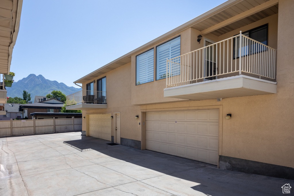 View of side of home featuring stucco siding, a balcony, a mountain view, an attached garage, and concrete driveway