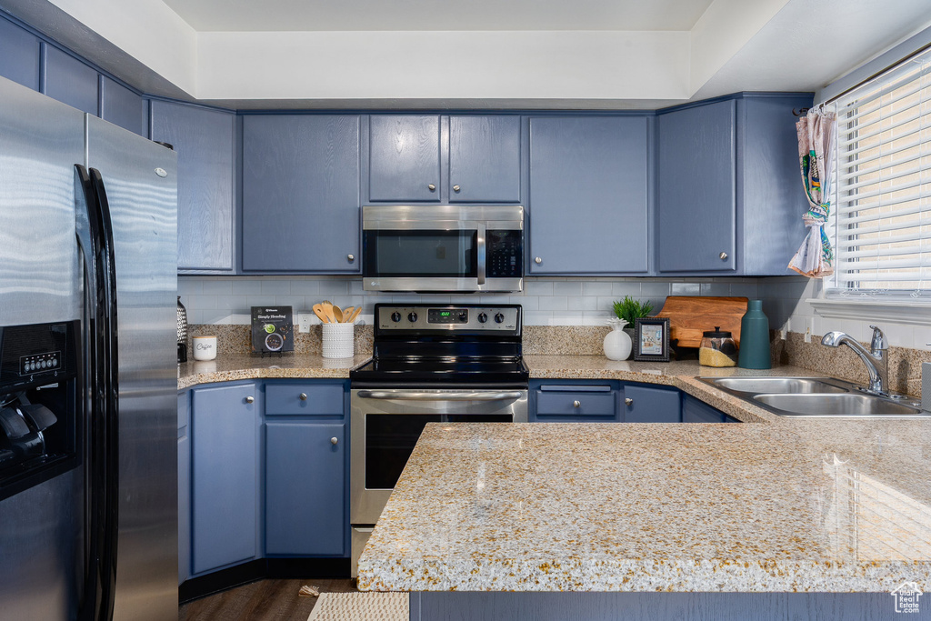 Kitchen featuring appliances with stainless steel finishes, a sink, blue cabinetry, and light countertops