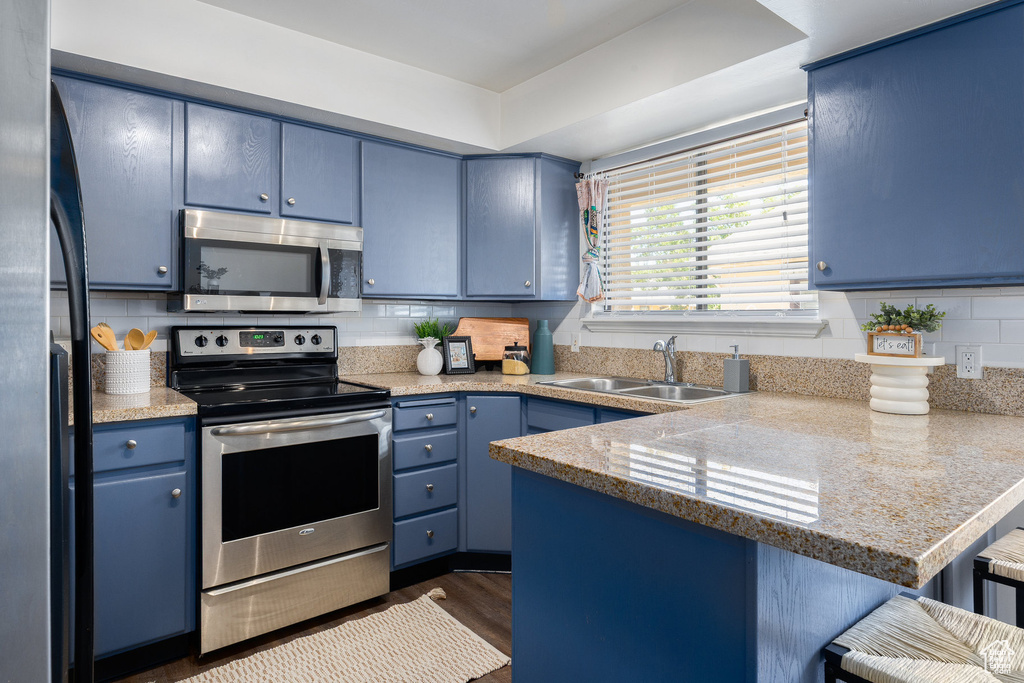 Kitchen featuring appliances with stainless steel finishes, blue cabinetry, a sink, and a peninsula