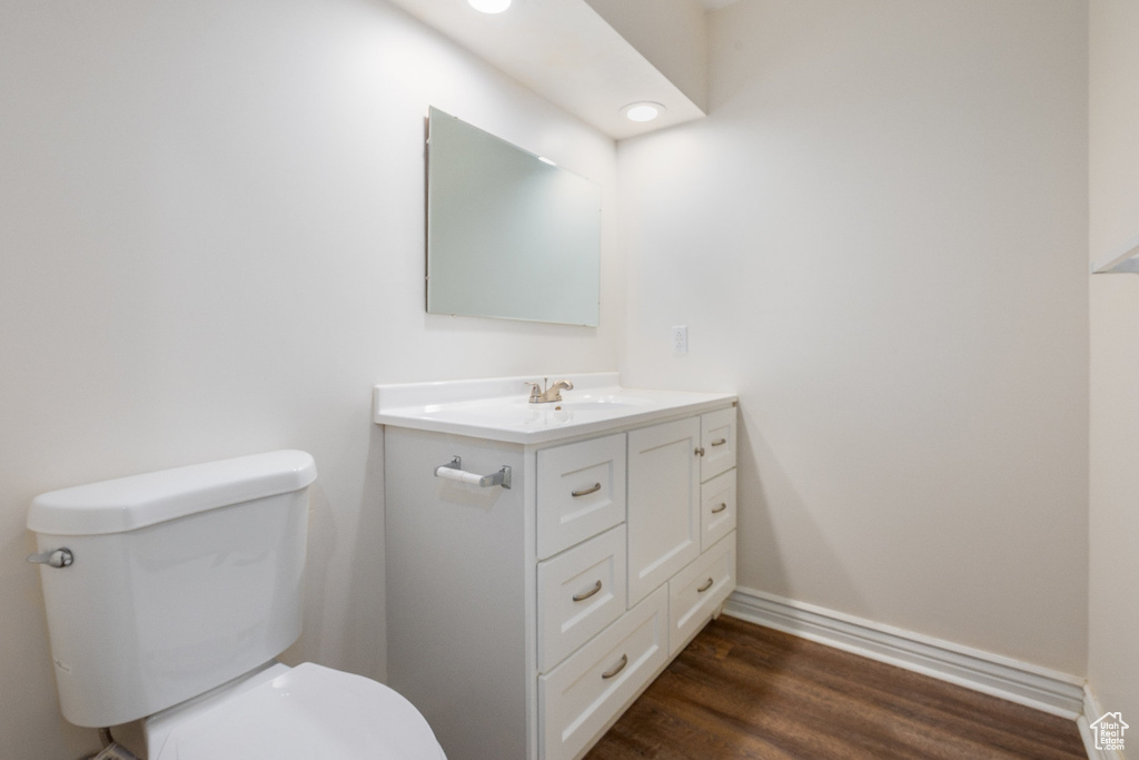 Half bathroom featuring vanity, toilet, wood finished floors, and baseboards