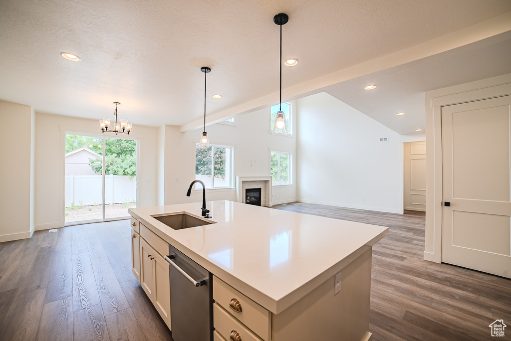 Kitchen with a sink, dishwasher, a glass covered fireplace, a chandelier, and dark wood-style floors