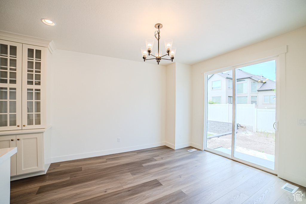 Unfurnished dining area with a chandelier, wood finished floors, baseboards, and recessed lighting