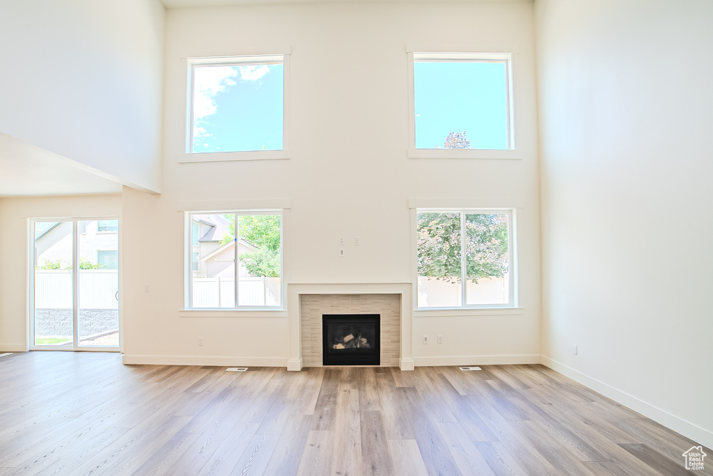 Unfurnished living room with a high ceiling, light wood-style floors, a fireplace, and baseboards