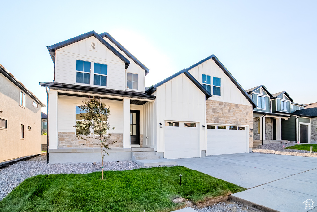 View of front of home featuring covered porch, board and batten siding, stone siding, concrete driveway, and an attached garage