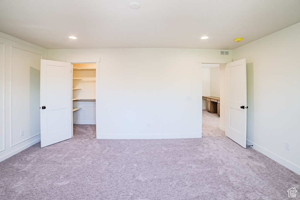 Unfurnished bedroom with light colored carpet, recessed lighting, baseboards, and a walk in closet