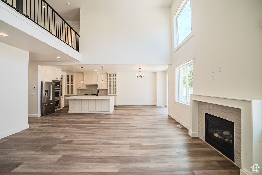 Unfurnished living room with a towering ceiling, a tile fireplace, a chandelier, wood finished floors, and baseboards