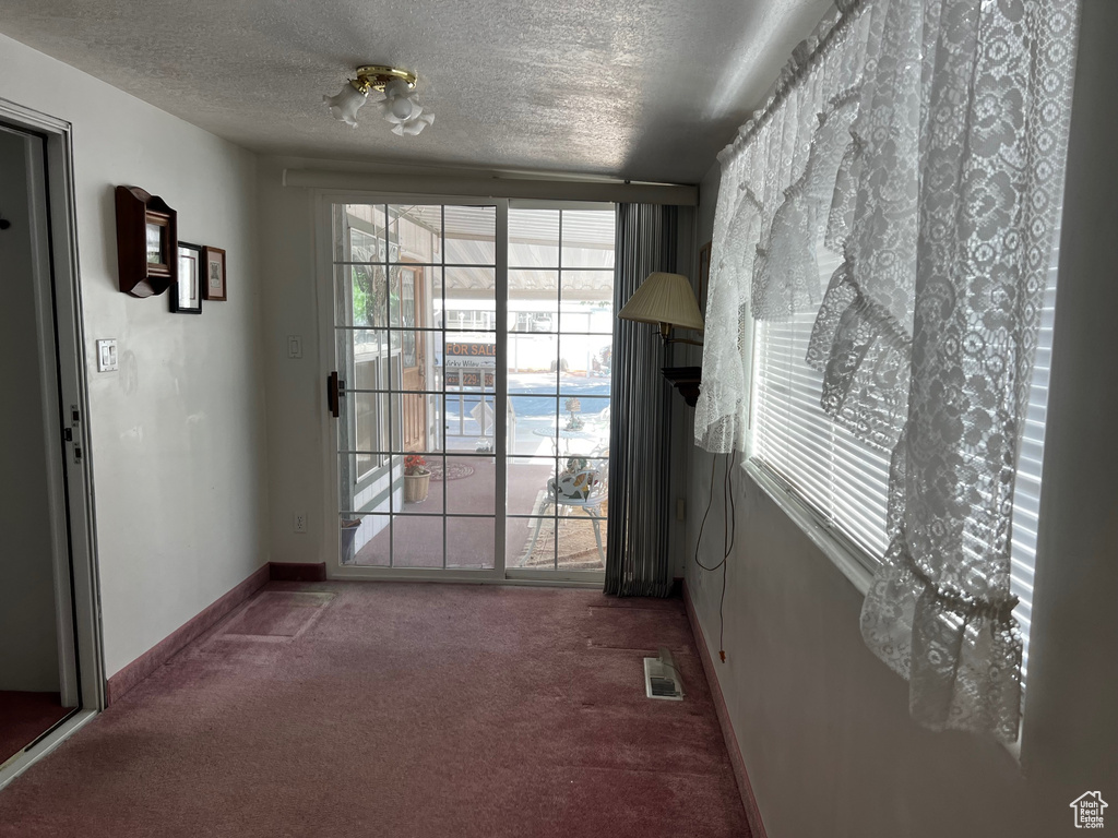 Doorway featuring carpet floors, a textured ceiling, and baseboards