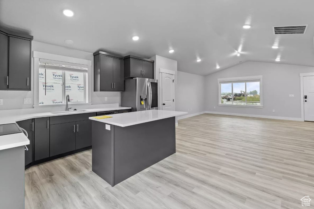 Kitchen with stainless steel fridge with ice dispenser, a sink, a kitchen island, light countertops, and vaulted ceiling