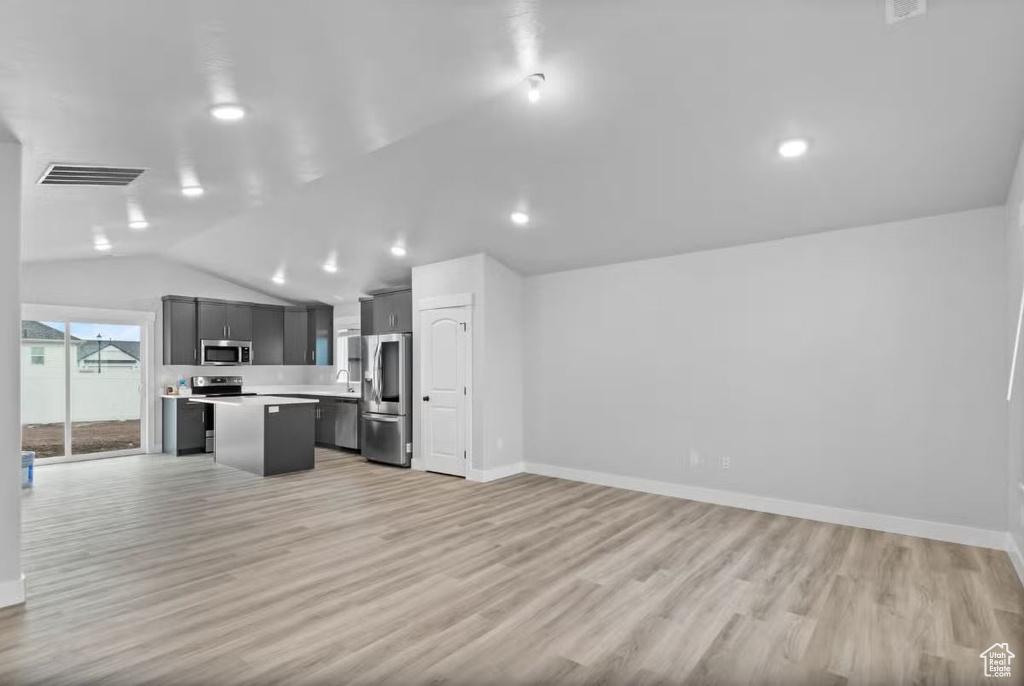 Kitchen with stainless steel appliances, open floor plan, a center island, light countertops, and vaulted ceiling