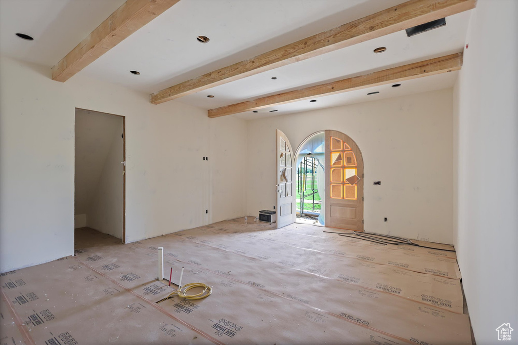 Empty room featuring arched walkways and beam ceiling