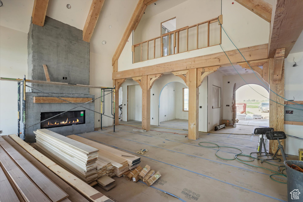 Unfurnished living room with high vaulted ceiling, a large fireplace, arched walkways, and beam ceiling
