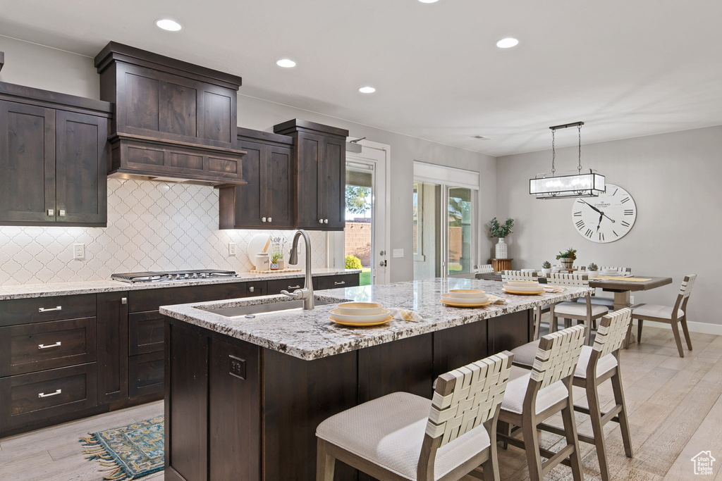 Kitchen with stainless steel gas cooktop, a sink, tasteful backsplash, light wood-type flooring, and light stone counters
