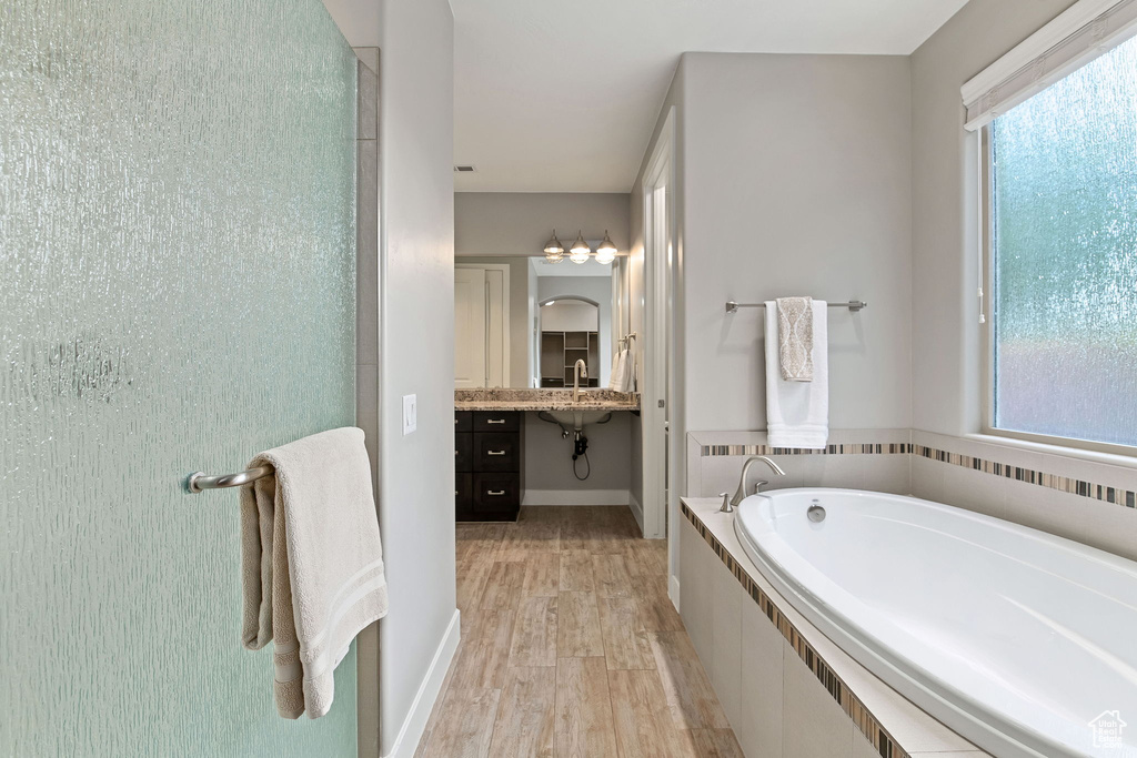 Bathroom with a bath, wood finished floors, baseboards, and vanity