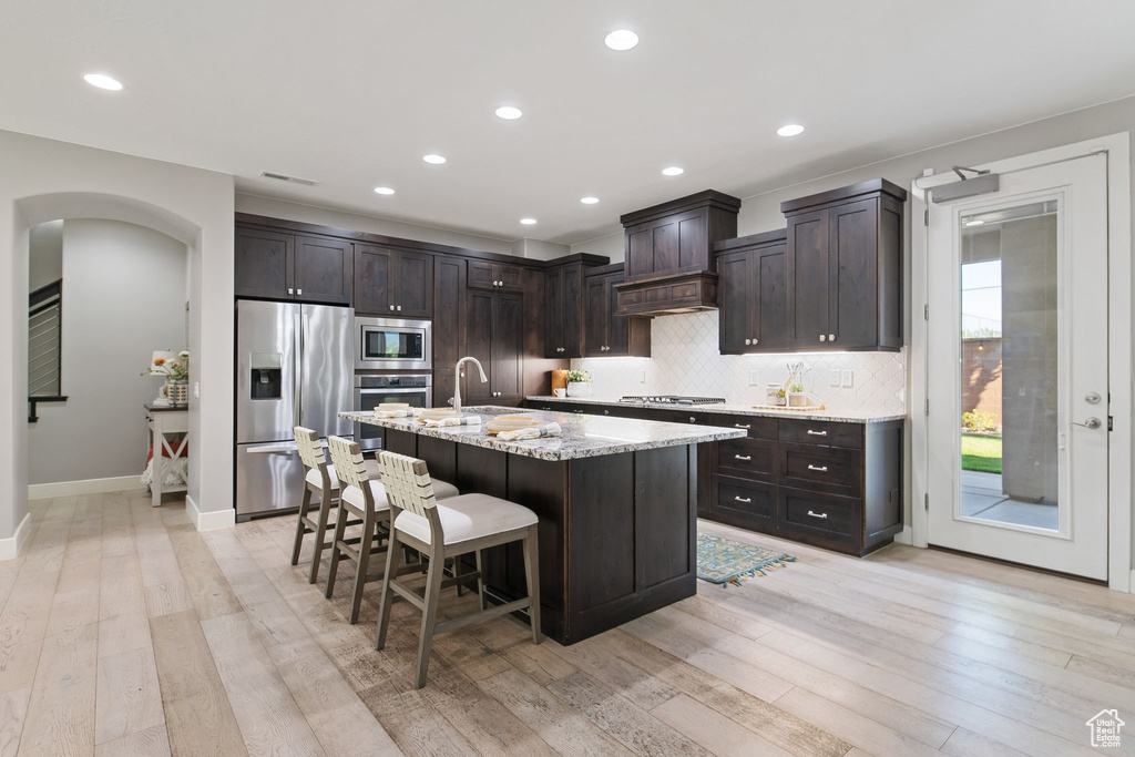 Kitchen with appliances with stainless steel finishes, arched walkways, a breakfast bar, light wood-style flooring, and decorative backsplash