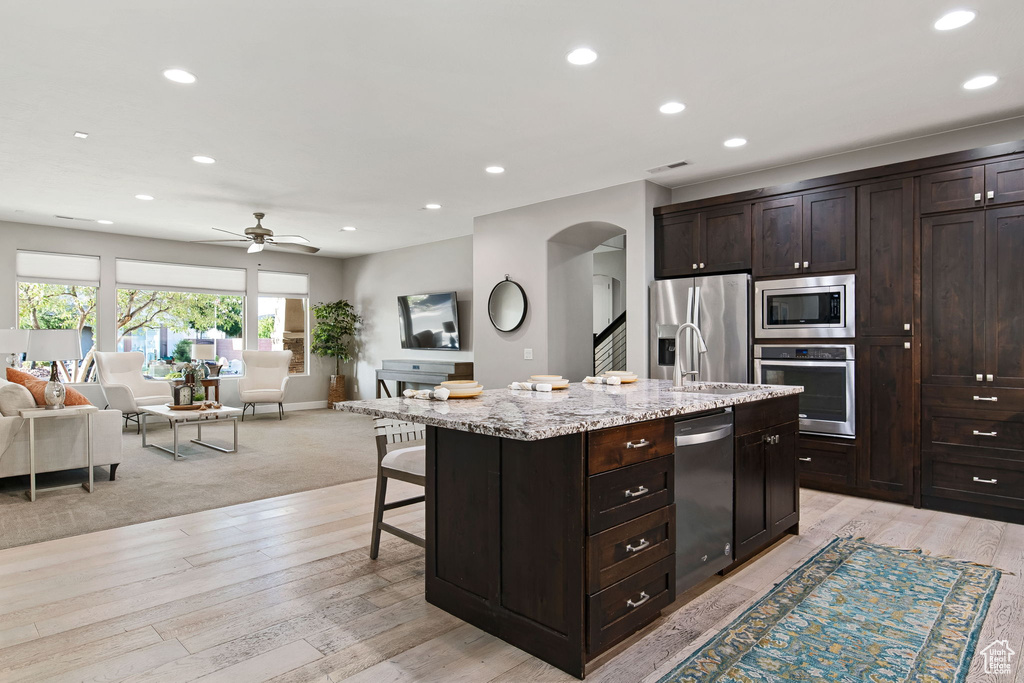 Kitchen with stainless steel appliances, arched walkways, open floor plan, recessed lighting, and light stone countertops