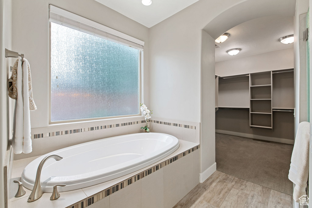 Bathroom with a bath, plenty of natural light, a walk in closet, and wood finished floors