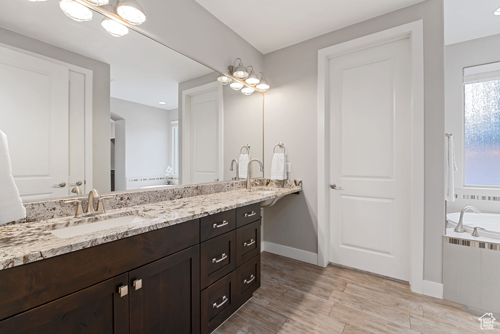 Bathroom featuring double vanity, a relaxing tiled tub, baseboards, and wood finished floors