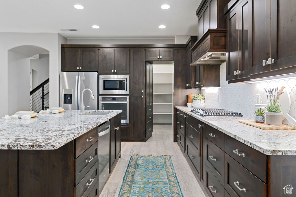 Kitchen with stainless steel appliances, dark brown cabinets, arched walkways, tasteful backsplash, and recessed lighting