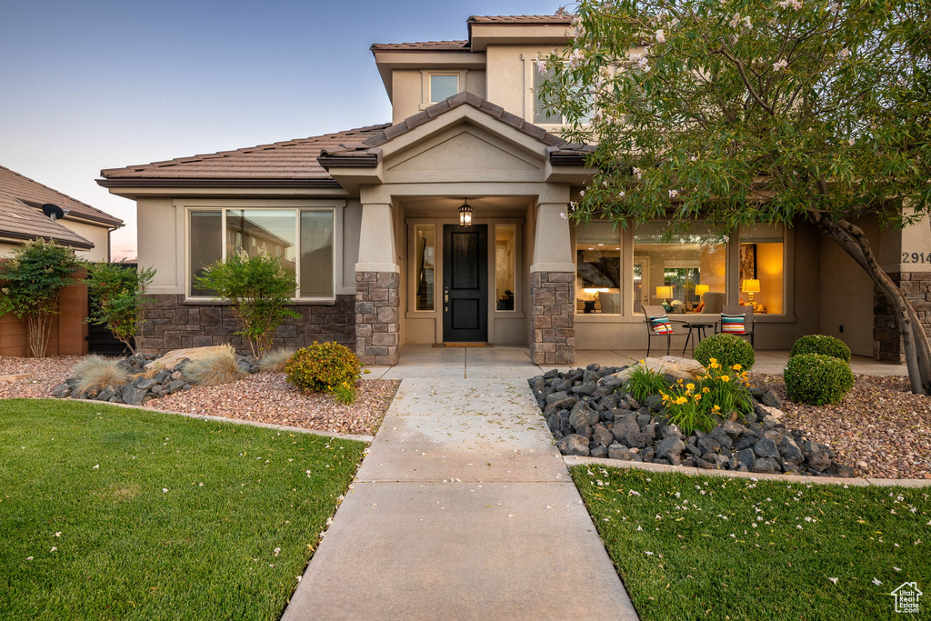 View of front of property featuring stucco siding, stone siding, a front lawn, and a tile roof