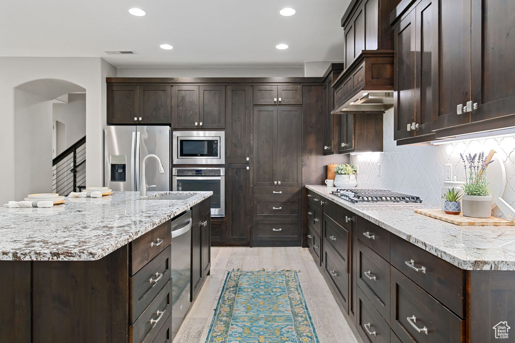 Kitchen featuring appliances with stainless steel finishes, dark brown cabinets, arched walkways, backsplash, and recessed lighting