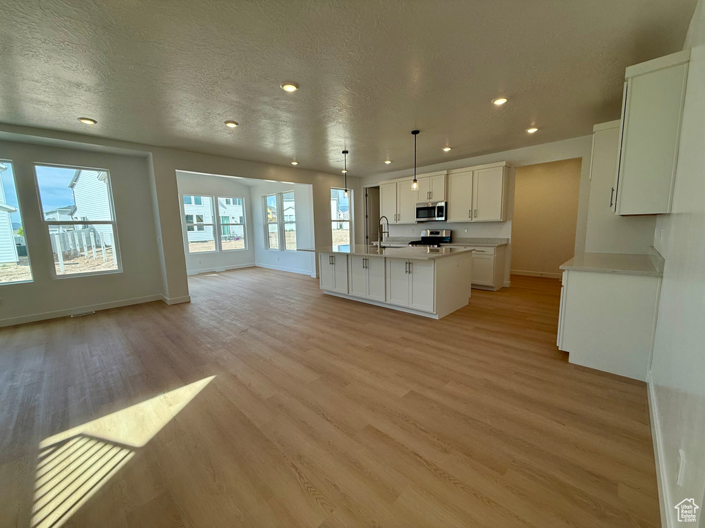 Kitchen with appliances with stainless steel finishes, open floor plan, light wood finished floors, a center island with sink, and white cabinetry