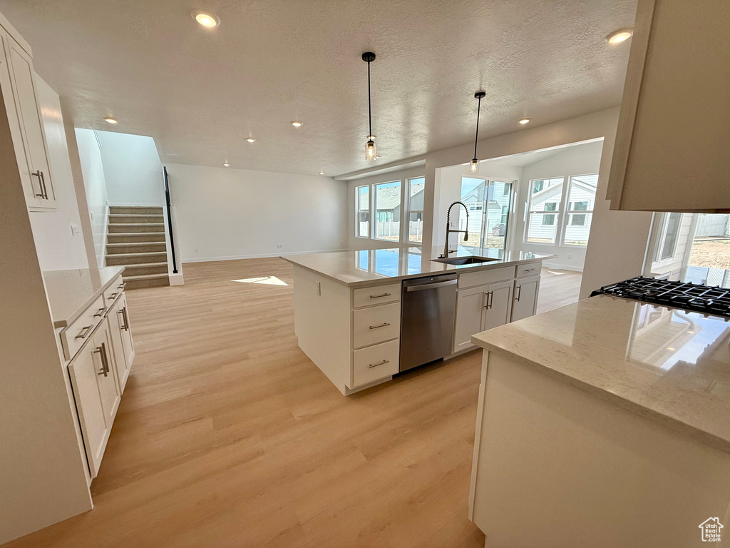 Kitchen featuring stainless steel dishwasher, open floor plan, light wood-type flooring, recessed lighting, and a kitchen island with sink