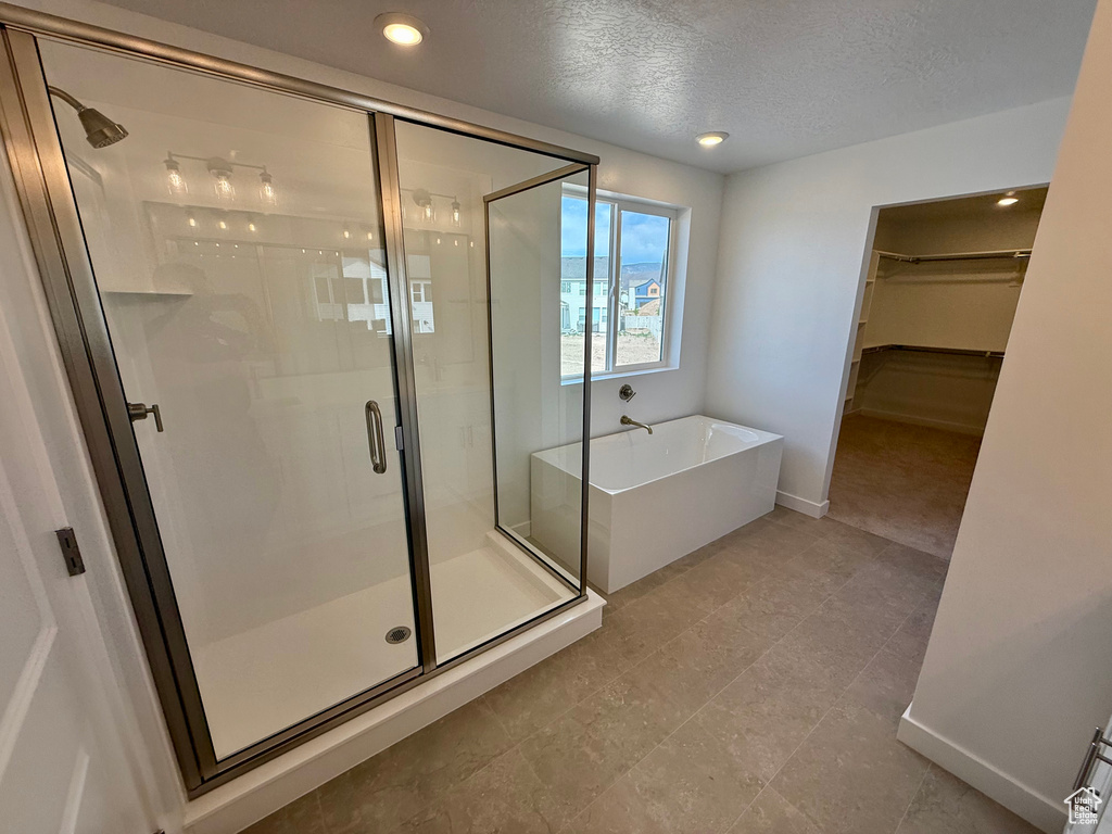 Bathroom with a soaking tub, a walk in closet, a shower stall, a textured ceiling, and recessed lighting