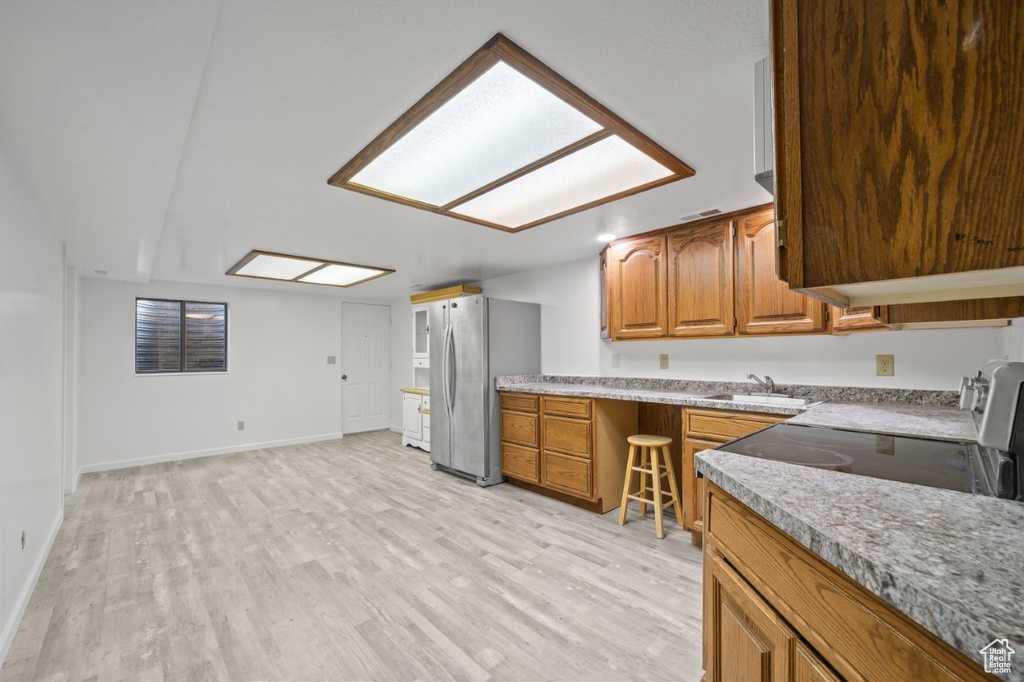Kitchen with freestanding refrigerator, brown cabinetry, light wood-style floors, and a sink