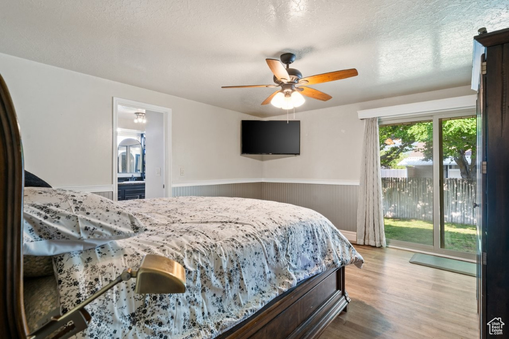Bedroom with access to exterior, wainscoting, wood finished floors, a ceiling fan, and a textured ceiling