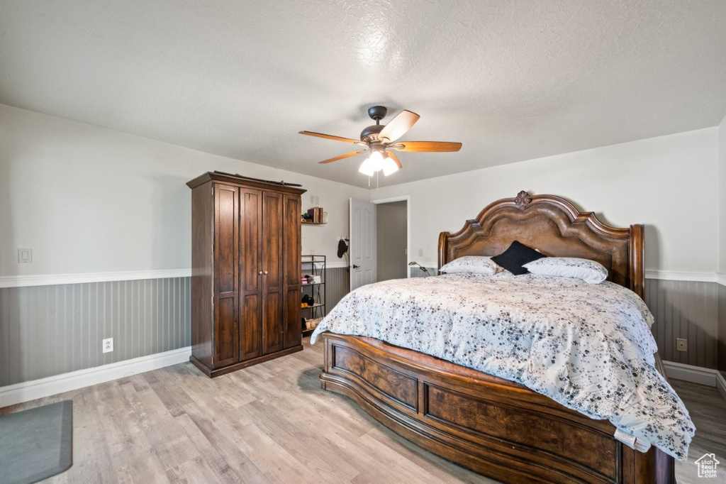 Bedroom featuring light wood finished floors, a wainscoted wall, a ceiling fan, and baseboards