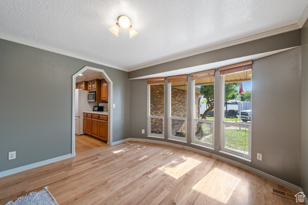 Unfurnished room featuring light wood-type flooring, crown molding, a textured ceiling, healthy amount of natural light, and baseboards