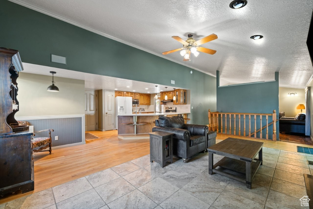 Living room featuring ornamental molding, ceiling fan, a textured ceiling, and light wood-style floors