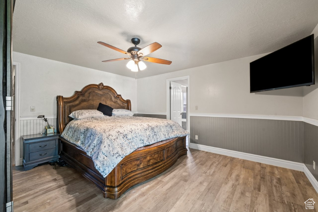 Bedroom with wainscoting, light wood-style floors, and a ceiling fan