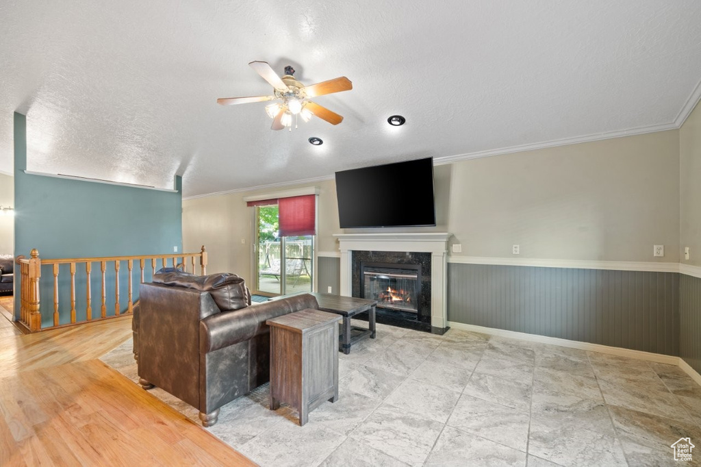 Living area featuring ceiling fan, wainscoting, a textured ceiling, a high end fireplace, and crown molding
