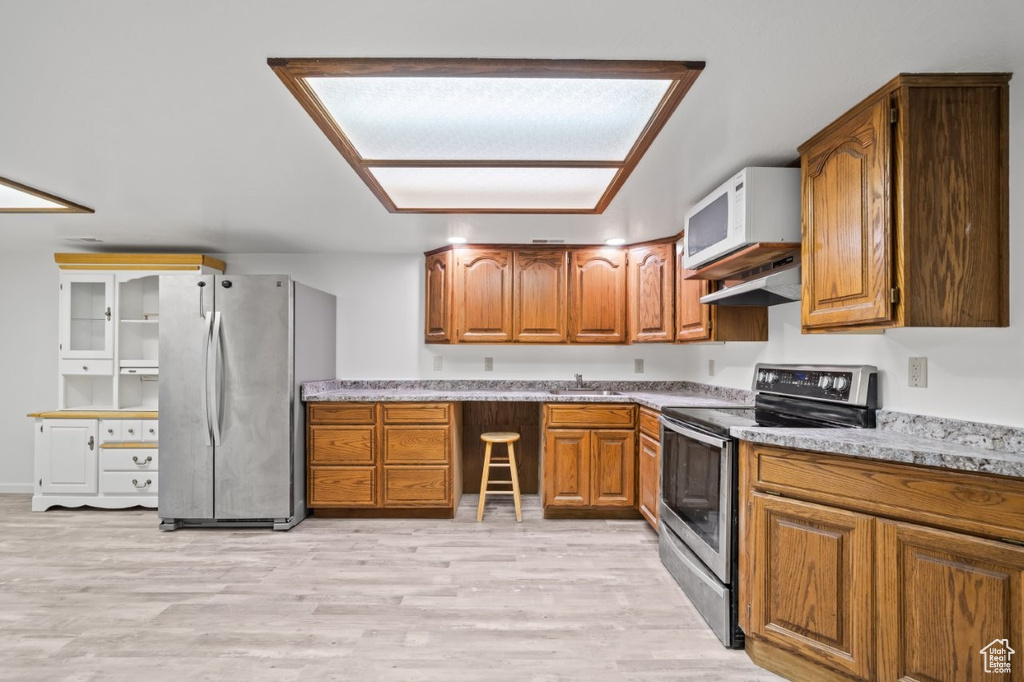 Kitchen with stainless steel appliances, a sink, brown cabinets, light wood-type flooring, and under cabinet range hood