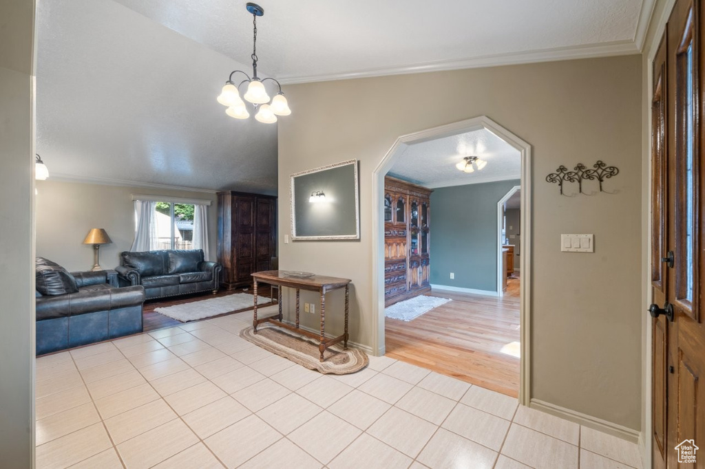 Living room with arched walkways, light tile patterned flooring, crown molding, baseboards, and a chandelier