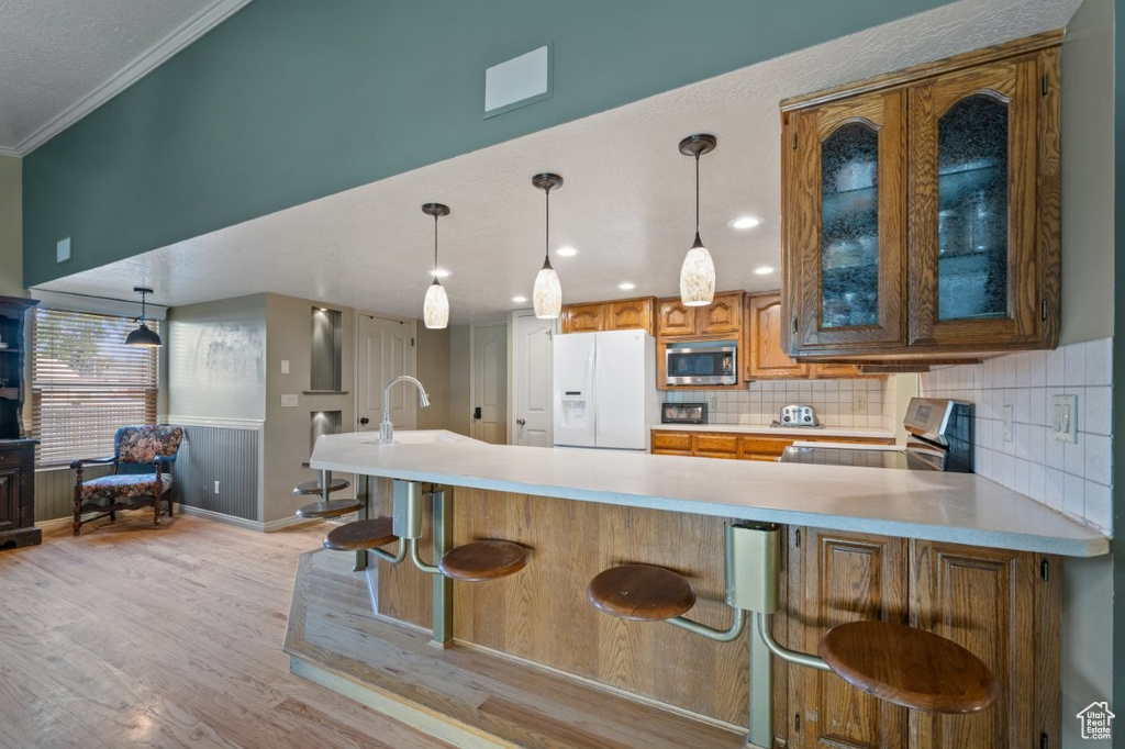 Kitchen with white refrigerator with ice dispenser, stainless steel microwave, stove, light countertops, and ornamental molding
