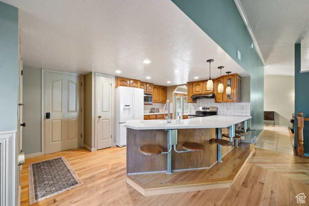 Kitchen featuring stainless steel appliances, a textured ceiling, brown cabinets, light countertops, and light wood finished floors