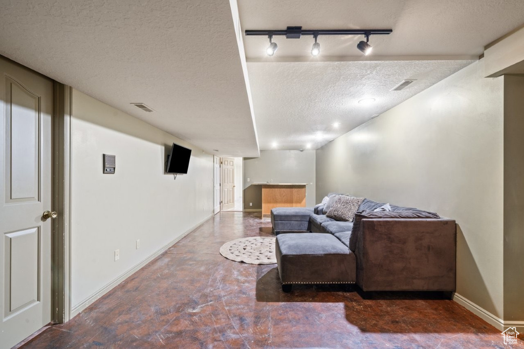Living area with rail lighting, baseboards, a textured ceiling, finished concrete flooring, and bar