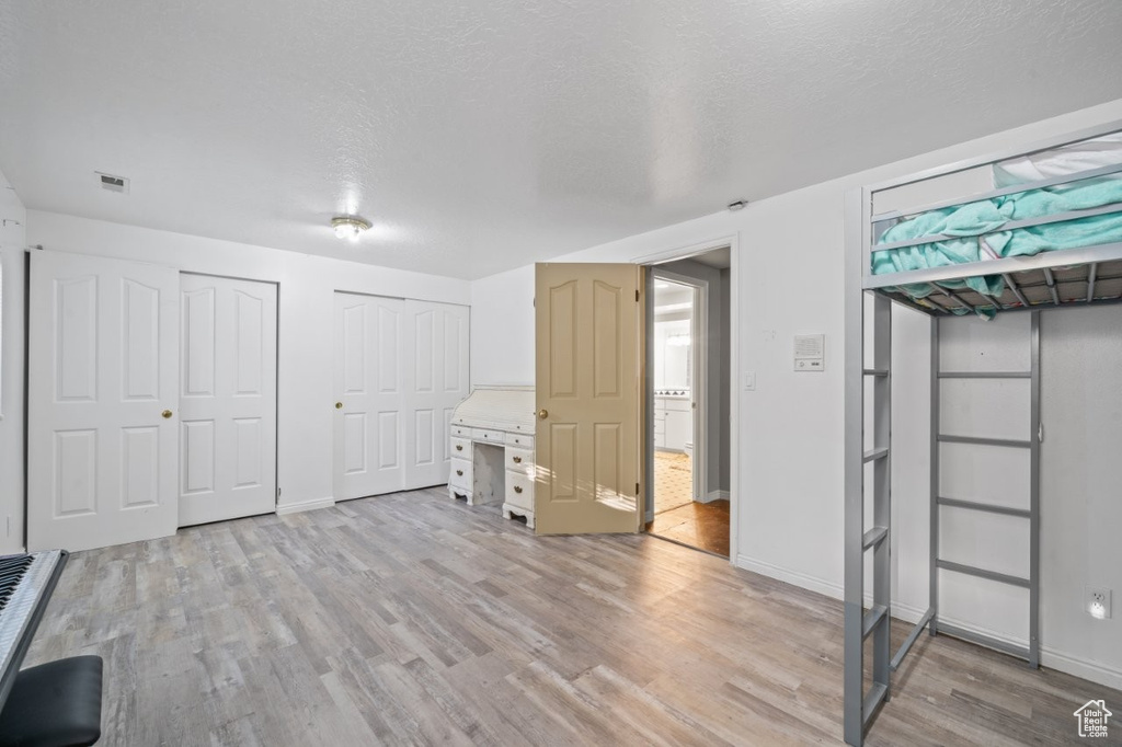 Unfurnished bedroom featuring multiple closets, light wood-type flooring, baseboards, and a textured ceiling