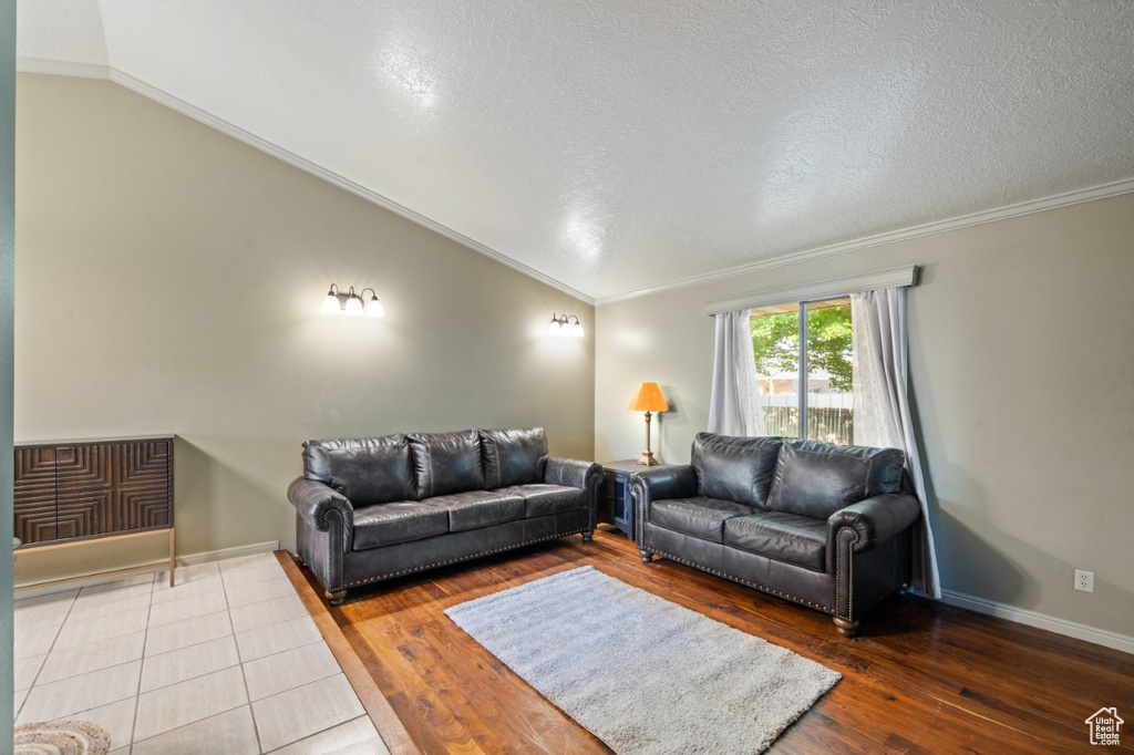 Living area featuring lofted ceiling, hardwood / wood-style floors, ornamental molding, a textured ceiling, and baseboards