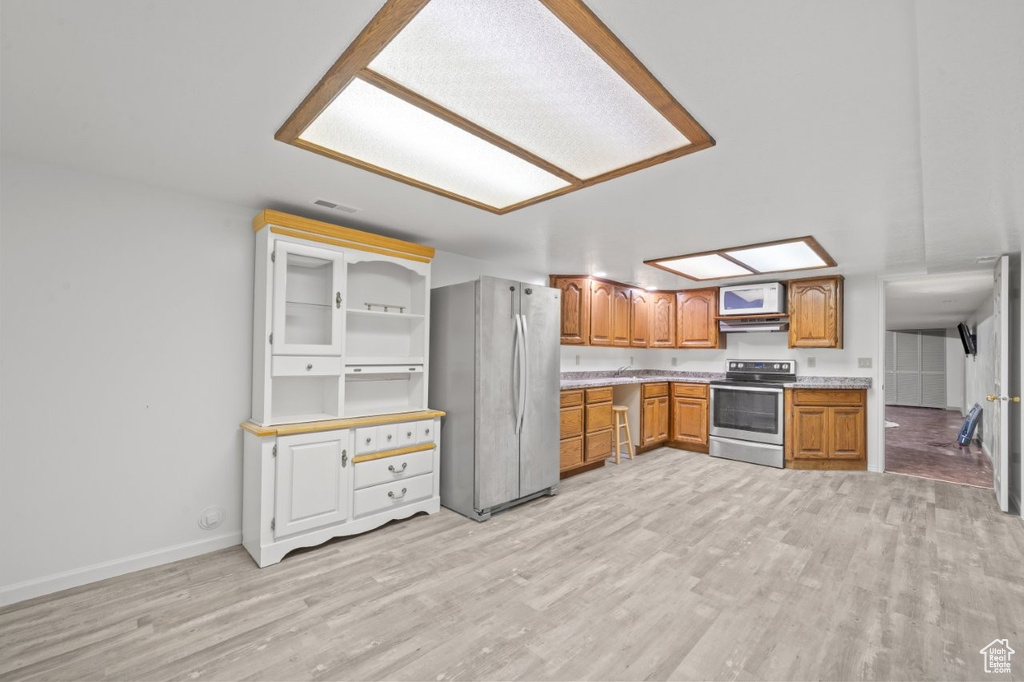 Kitchen featuring appliances with stainless steel finishes, light wood finished floors, brown cabinets, light countertops, and baseboards