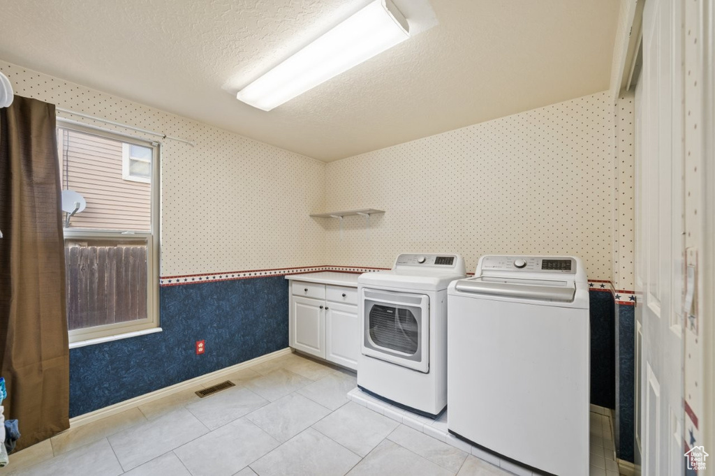 Laundry area featuring cabinet space, wallpapered walls, a textured ceiling, washer and clothes dryer, and baseboards
