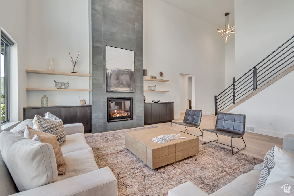 Living room featuring a towering ceiling, plenty of natural light, stairs, wood finished floors, and a fireplace
