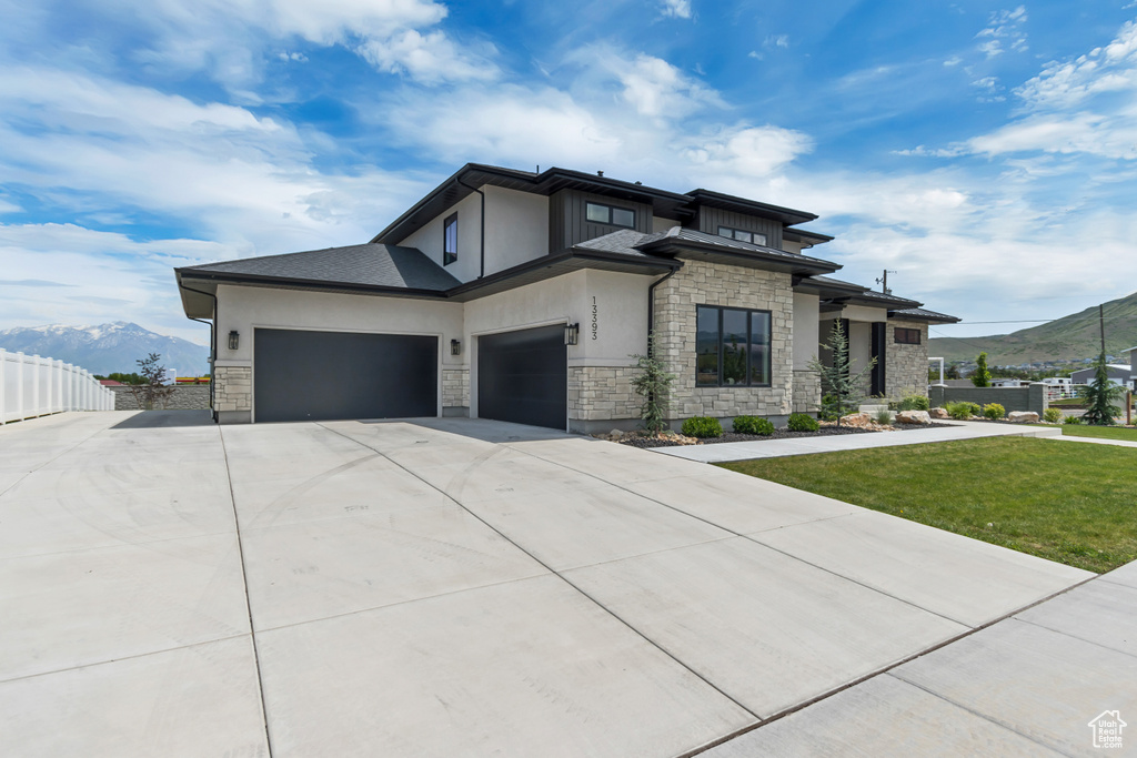 View of front of home with stone siding, concrete driveway, stucco siding, a mountain view, and an attached garage