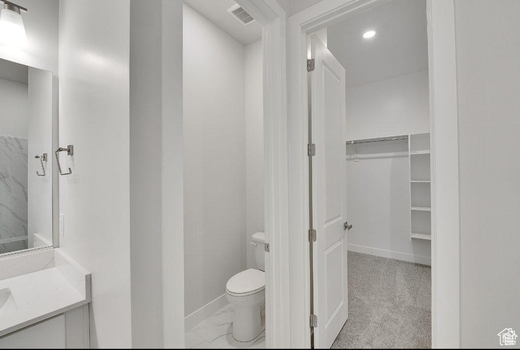 Bathroom featuring toilet, vanity, baseboards, marble finish floors, and a spacious closet